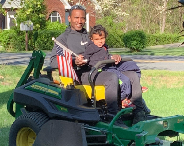 hope lawn care owner on lawn mower with son holding an american flag